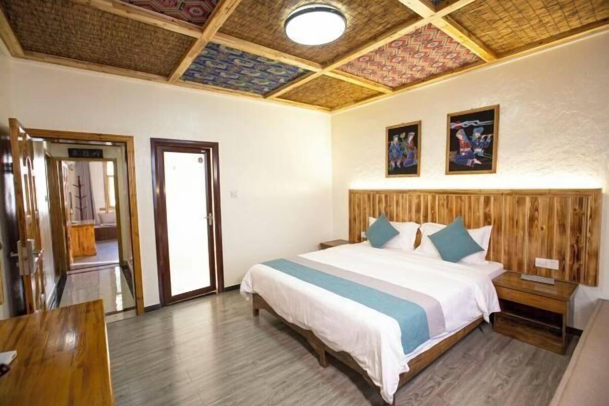 Een slaapkamer met een houten hoofdbord, een bed met wit beddengoed, een nachtkastje en een houten bankje.