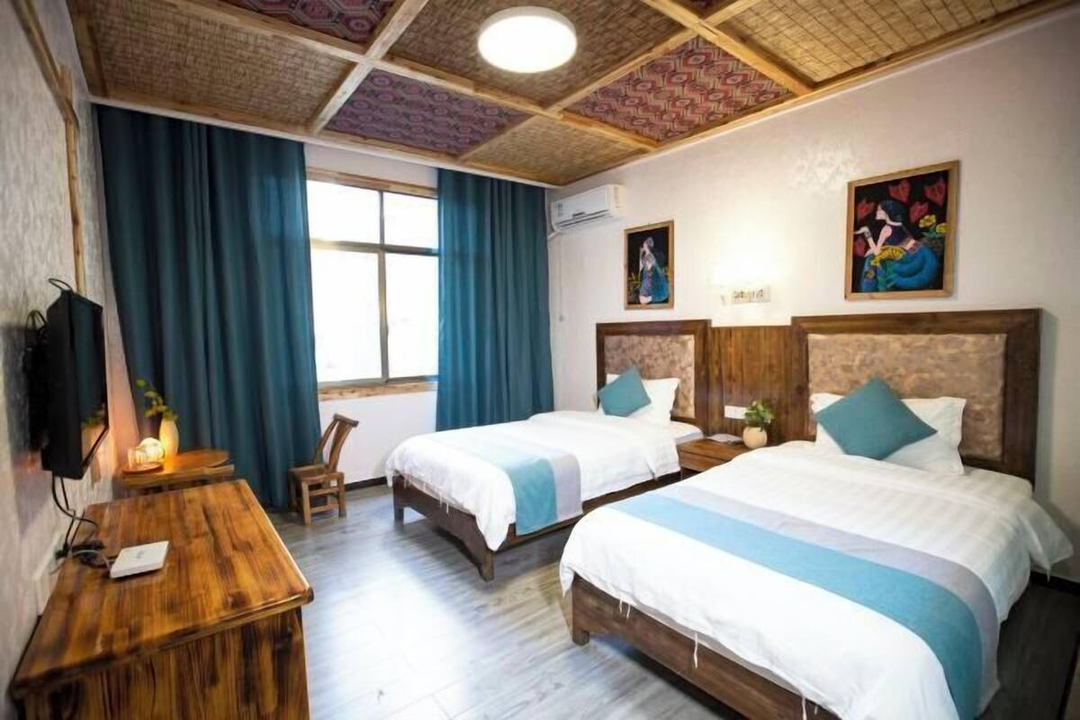 Een hotelkamer met twee bedden, een houten bureau, een televisie en een raam met gordijnen.