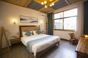 Une chambre avec un grand lit, un plancher en bois, un tableau au mur et une fenêtre avec des rideaux.