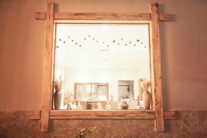 Een spiegel met houten lijst, die een kamer weerspiegelt met een raam, een vaas en een plant.
