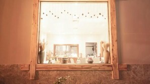 Een spiegel met houten lijst, die een kamer weerspiegelt met een stenen muur, een raam en meubilair.