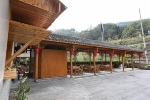 Ein hölzernes Pavillon mit Ziegeldach, Sitzgelegenheiten im Freien und einem mit Steinplatten gepflasterten Bereich.