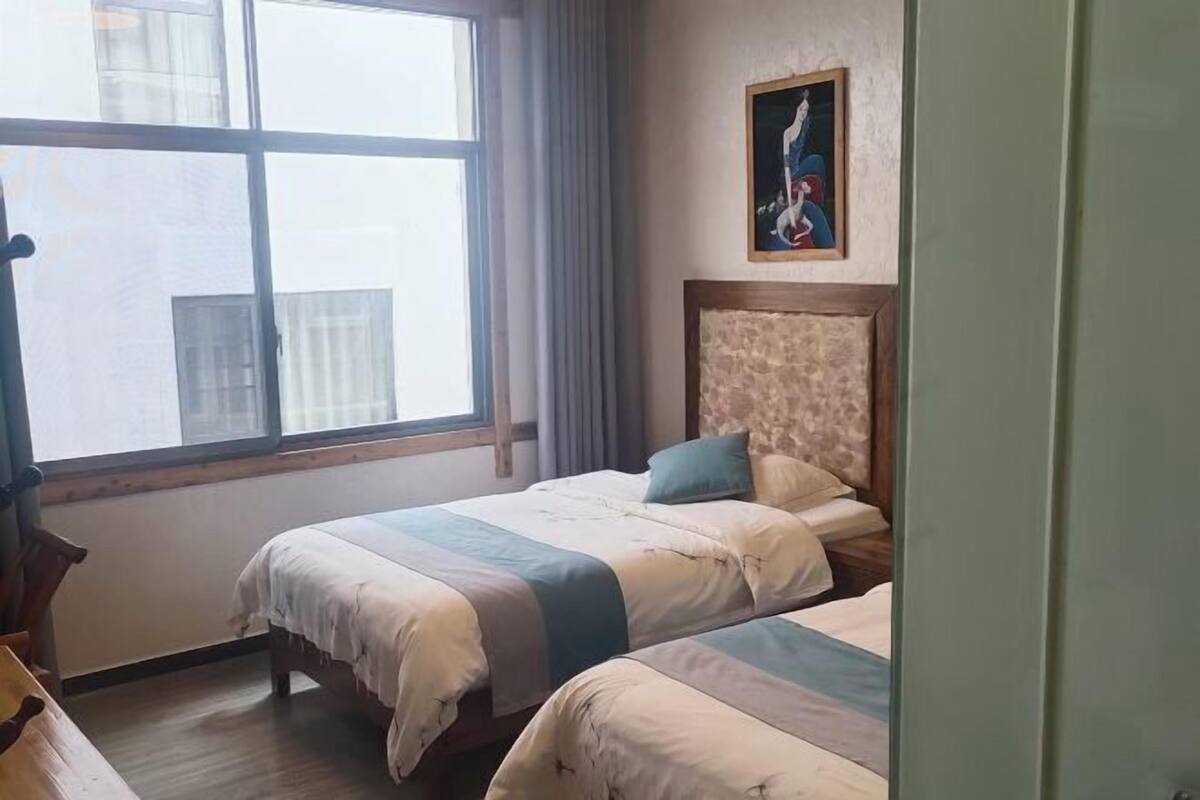 Een hotelkamer met twee bedden, een groot raam, een schilderij aan de muur en een houten hoofdeinde.