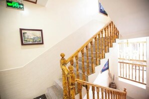 Un escalier en bois avec une rampe, un tableau encadré au mur et une fenêtre avec des barreaux.