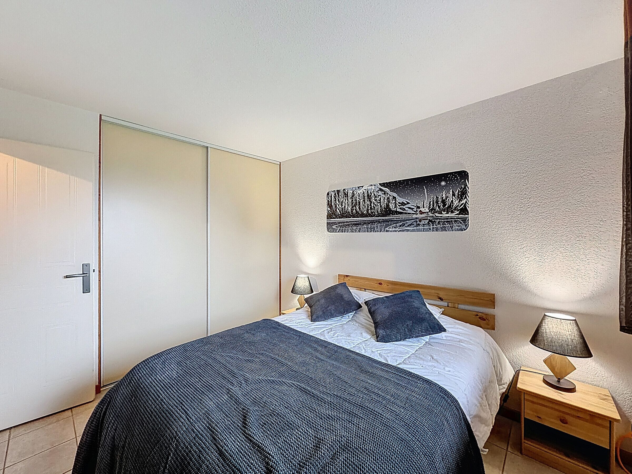 Een slaapkamer met een bed, twee nachtkastjes, een deur en een kunstwerk aan de muur.