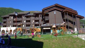 A multi-story hotel with balconies, a playground, and a mountain backdrop.