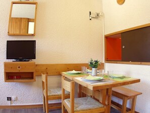 A wooden dining table with chairs, a television, a small cabinet, and a wall-mounted mirror. - Divisible studio in Valmorel, 4 people, west balcony, optional parking (Valmorel)
