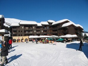 A ski resort with wooden buildings, a covered outdoor seating area, and snow-covered slopes. - Divisible studio in Valmorel, 4 people, west balcony, optional parking (Valmorel)
