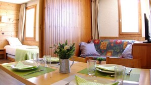 A cozy room with a wooden floor, a bed, a sofa, and a dining table set with plates, glasses, and a pitcher of flowers.