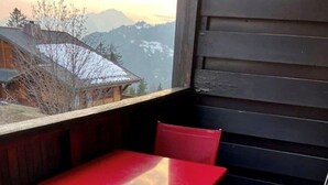 Un tavolo e sedie rossi su un balcone con vista sulle montagne.