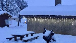 Zona all'aperto ricoperta di neve, con un tavolo da picnic e una statua di una mucca.