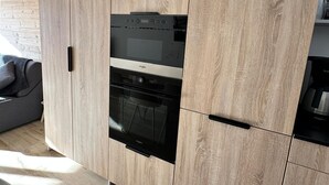 A kitchen with a built-in oven and microwave, wooden cabinetry, and a grey sofa in the adjacent living area. - 2-room apartment in Châtel, sleeps 5 with WIFI and pets welcome (Châtel)