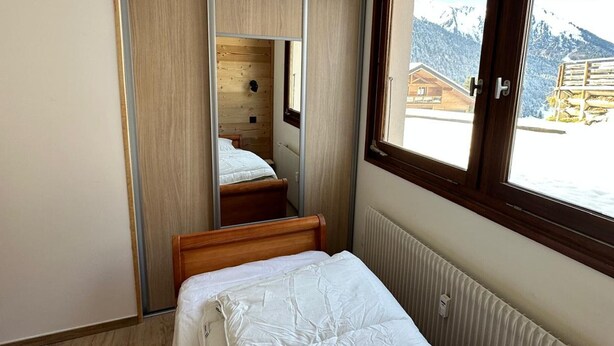 Une chambre à coucher avec une armoire en bois, un lit et une fenêtre donnant sur des montagnes enneigées.