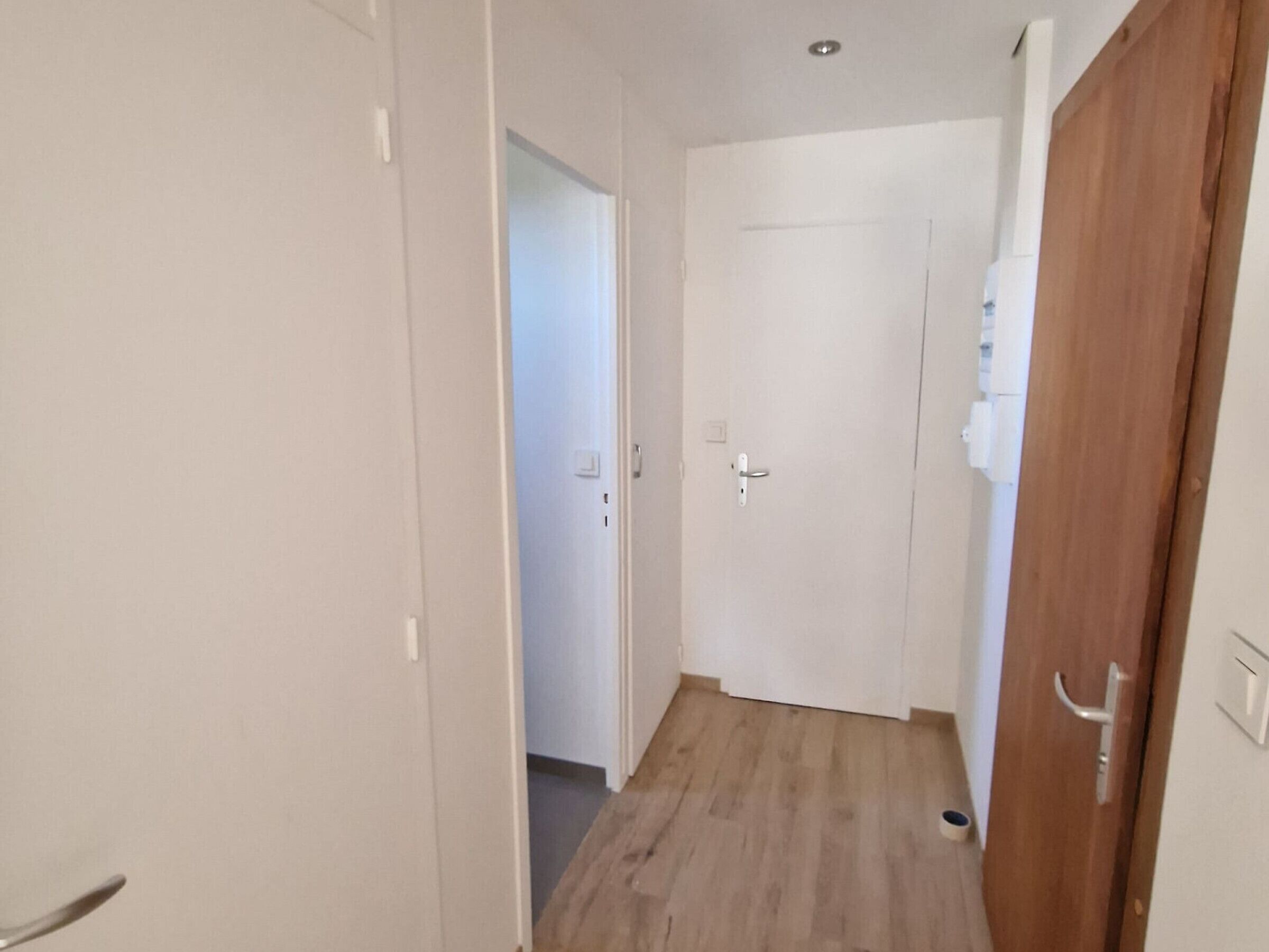 A narrow hallway with wooden flooring and white walls.
