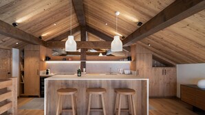 A modern kitchen with wooden beams, a central island with stools, pendant lighting, and built-in appliances. - Apartment for 10 people with sauna in Saint-Martin-de-Belleville (Saint-Martin-de-Belleville)