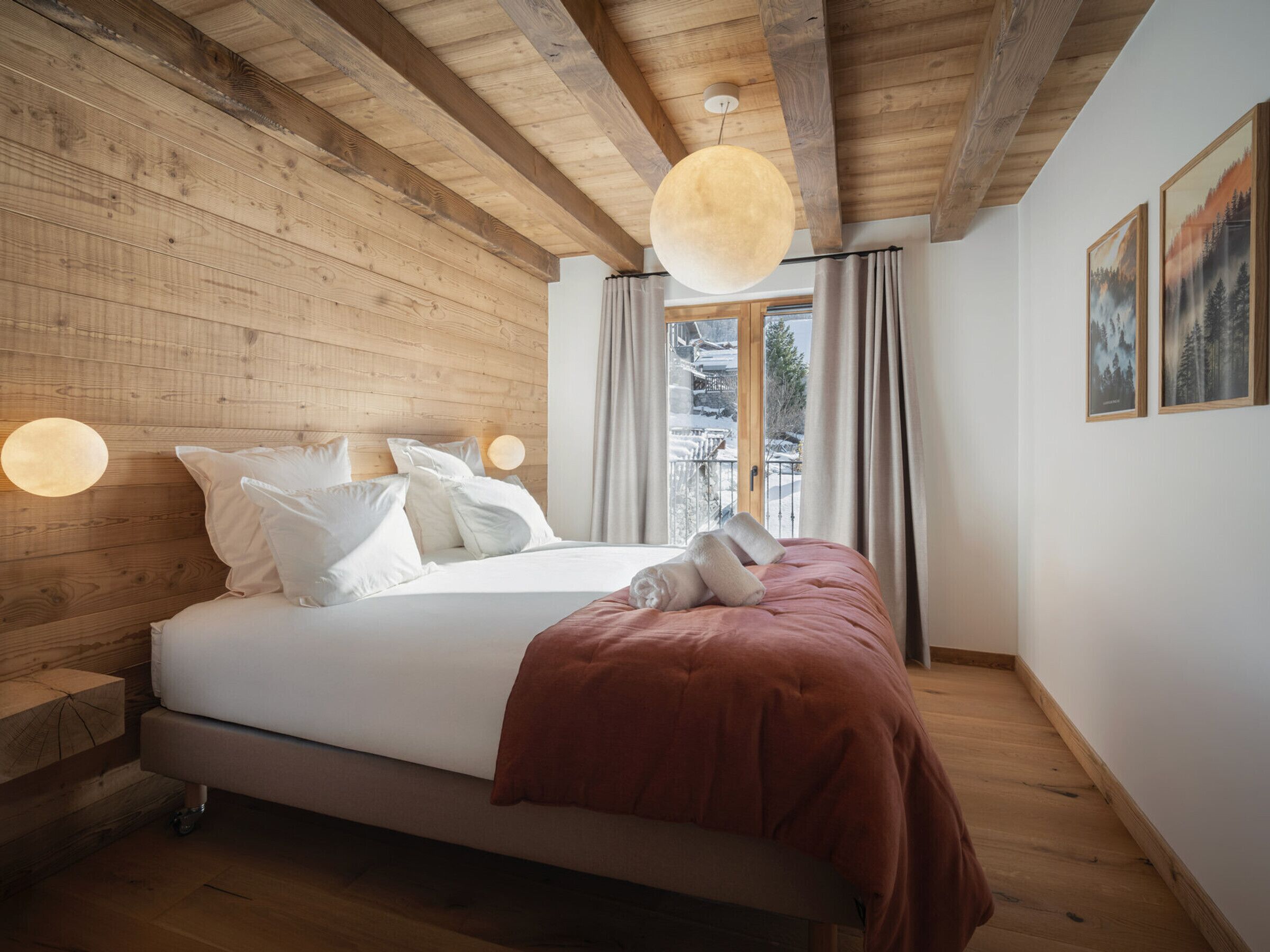 A wooden-paneled bedroom with a bed, two wall-mounted lights, and a window with curtains.