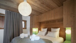 A wooden-paneled bedroom with a large bed, two bedside lamps, and a hanging light fixture. - Charming apartment for 4 near center (Saint-Martin-de-Belleville)