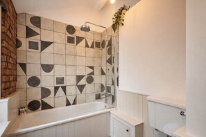 Une salle de bain avec un mur recouvert de carreaux aux motifs géométriques, une douche et un meuble-lavabo blanc avec des toilettes.