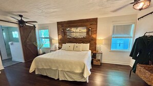 A bedroom with a large bed, wooden headboard, a ceiling fan, and a window with blinds.