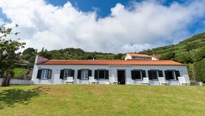 Un bâtiment blanc avec un toit recouvert de tuiles rouges, de nombreuses fenêtres dotées de volets et plusieurs chaises blanches devant.