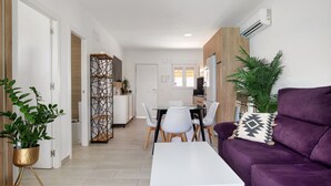 A modern living room with a purple sofa, a white coffee table, and a dining area with a white table and chairs. - Holiday Home 'Casita Dana' with Private Pool, Wi-Fi and Air Conditioning (Conil de la Frontera)