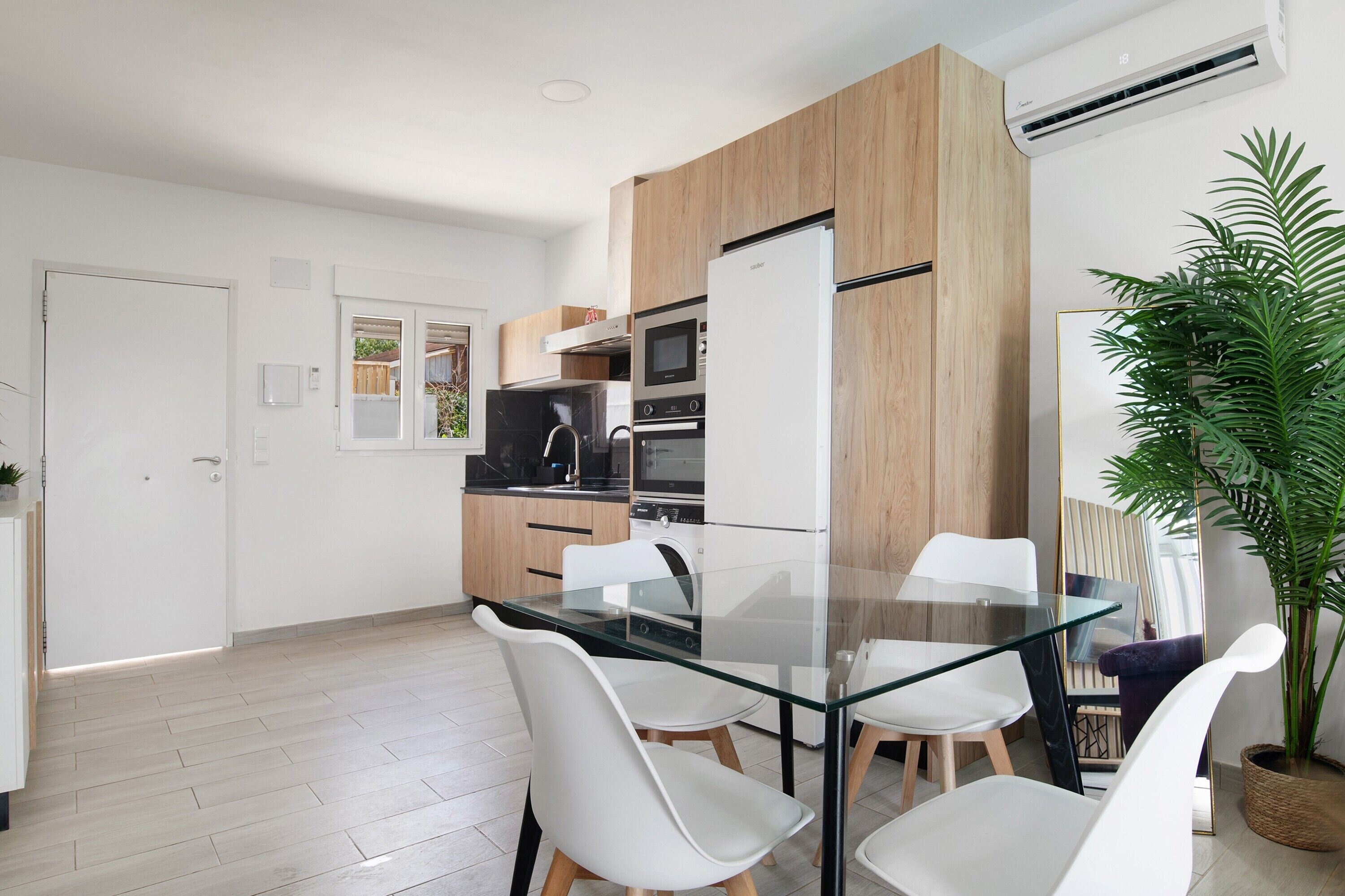 A modern kitchen with a glass dining table, white chairs, and a built-in oven.