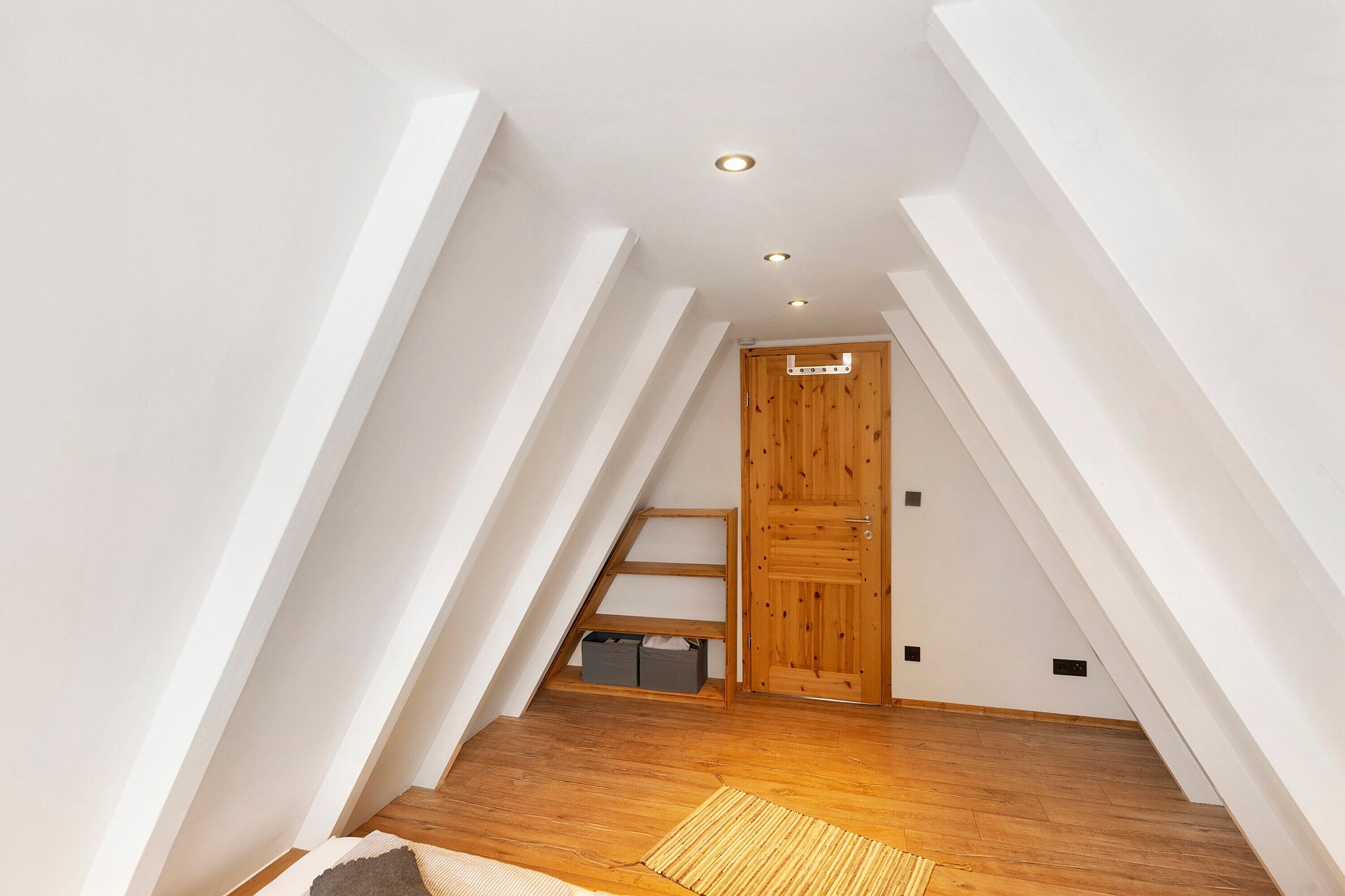 A sloped ceiling attic room with wooden flooring, a door, and a small shelf.