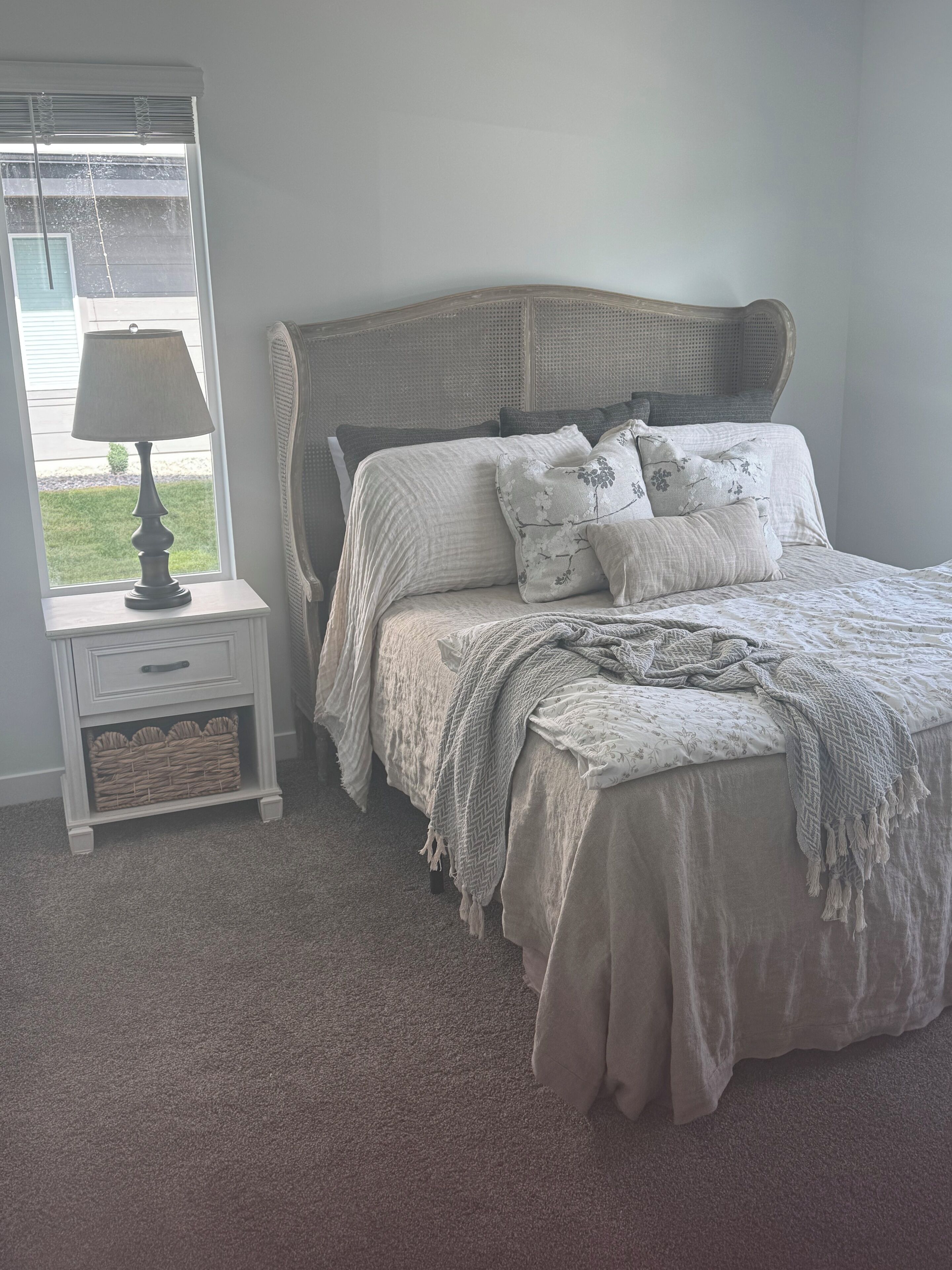 A bedroom with a bed, a nightstand, a lamp, and a window.