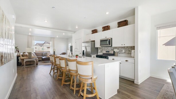 A modern kitchen with white cabinetry, a central island with bar stools, and a view to the living area. -  New townhome, quick freeway & public trans. access, seasonal pool & pickleball. (American Fork)