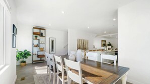 A modern dining area with a wooden table and white chairs, a kitchen in the background, and a potted plant on the left. -  New townhome, quick freeway & public trans. access, seasonal pool & pickleball. (American Fork)