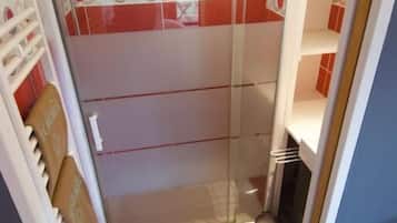A compact bathroom with a shower, a toilet, and a small storage area.