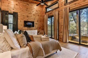 A wooden-paneled bedroom with a bed, a TV, and a view of a hot tub outside.