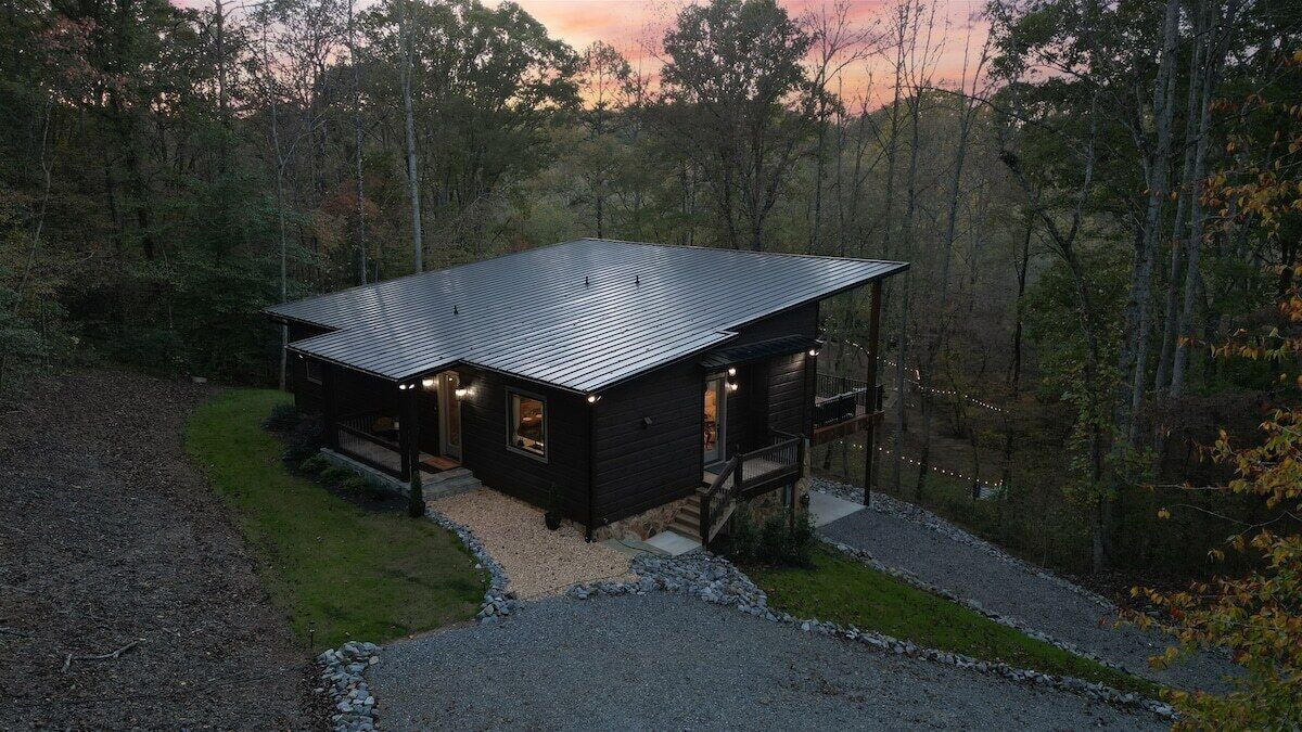 Une cabane avec un toit en métal, une terrasse et une allée gravillonnée.