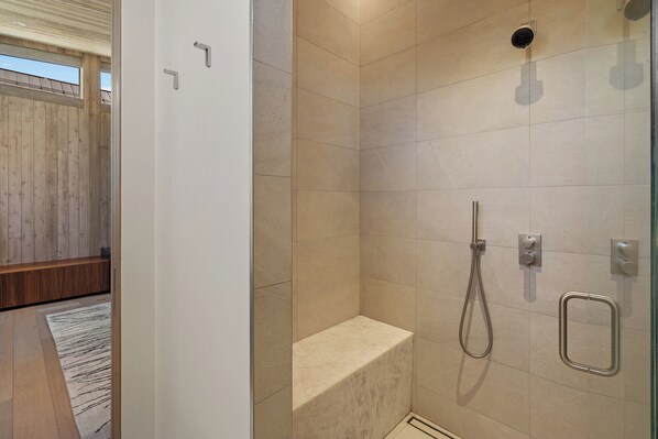 A modern bathroom with a shower, a bench, and a glass door.