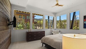 A bedroom with a large bed, a dresser, and a nightstand. There are multiple windows offering a view of a mountainous landscape.