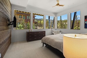 Une chambre à coucher avec un grand lit, une commode et une table de chevet. Plusieurs fenêtres offrent une vue sur un paysage montagneux.