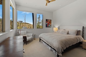 A bedroom with a large bed, a desk, and two windows offering a view of trees and a clear sky. - Monteluce by Exceptional Stays (MOUNTAIN VILLAGE)