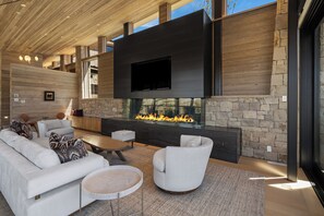 A modern living room with a stone fireplace, a flat-screen TV, and a large window.