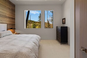 A bedroom with a bed, two windows, a dresser, and a lamp.
