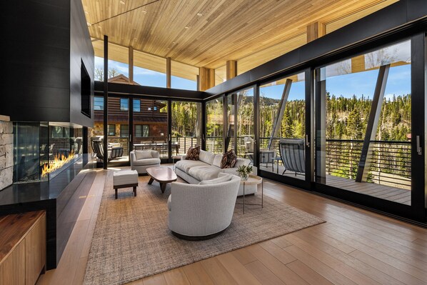 A modern interior with a fireplace, seating area, and large windows offering a view of the outdoors.
