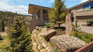 A modern building with a stone facade, large windows, and a wooden deck overlooking a forested area.