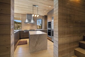Une cuisine moderne dotée d’un îlot central, d’appareils électroménagers en acier inoxydable et de panneaux en bois.