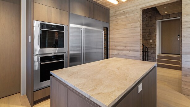 A modern kitchen with stainless steel appliances, wooden cabinetry, and a marble countertop.
