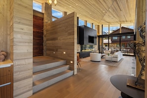 A modern interior with a wooden staircase, a fireplace, and a view of the mountains.
