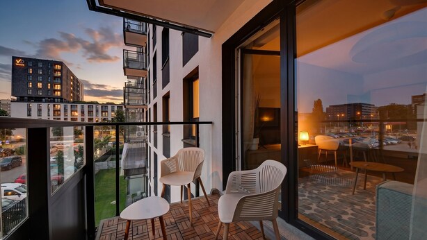 A balcony with two chairs and a table, a view of a cityscape, and a building with a 'Wave' sign. - RentPlanet - Apartament Braniborska IV (Wrocław)