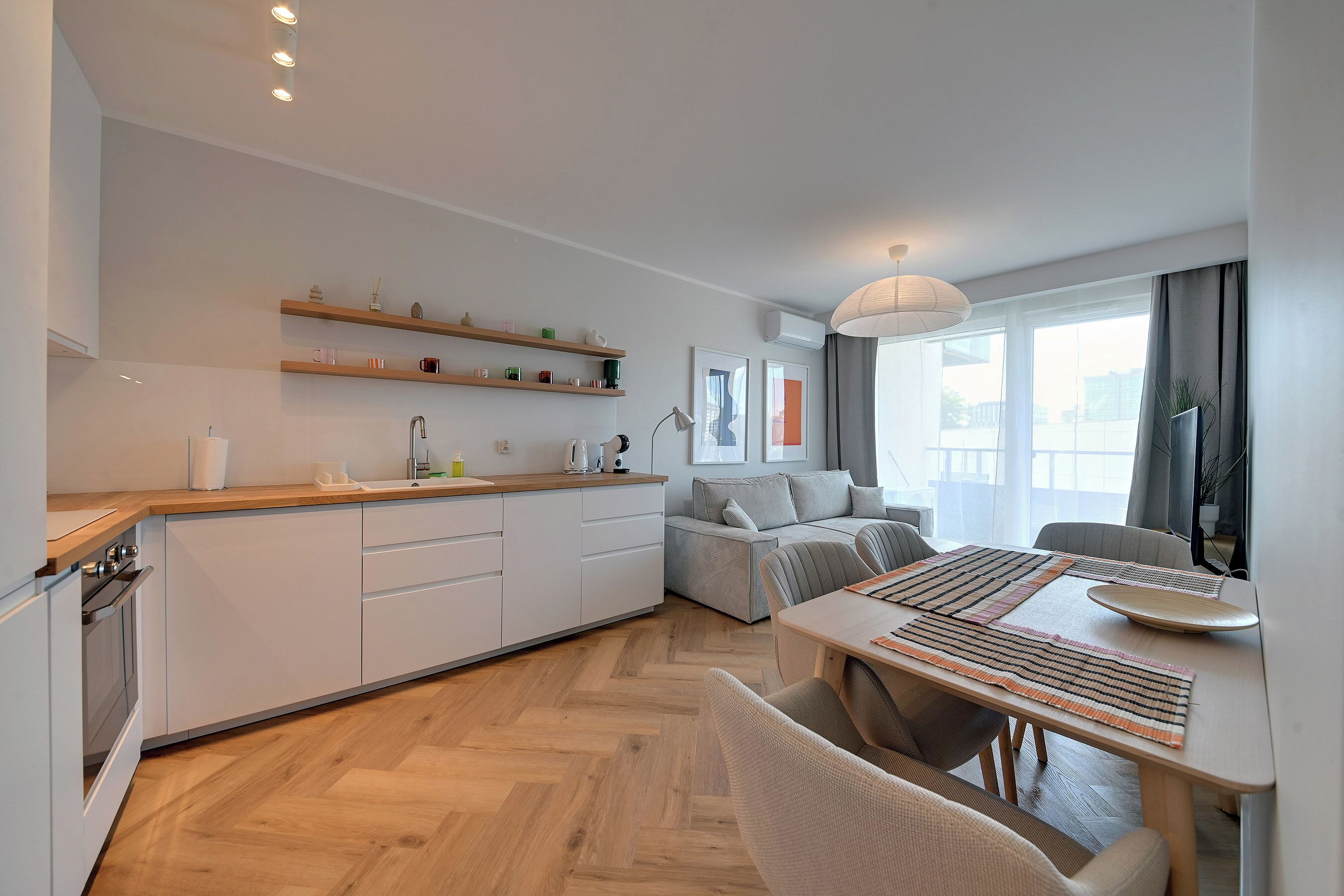 A modern kitchen with wooden cabinets, a dining table with chairs, and a sofa in the living area.