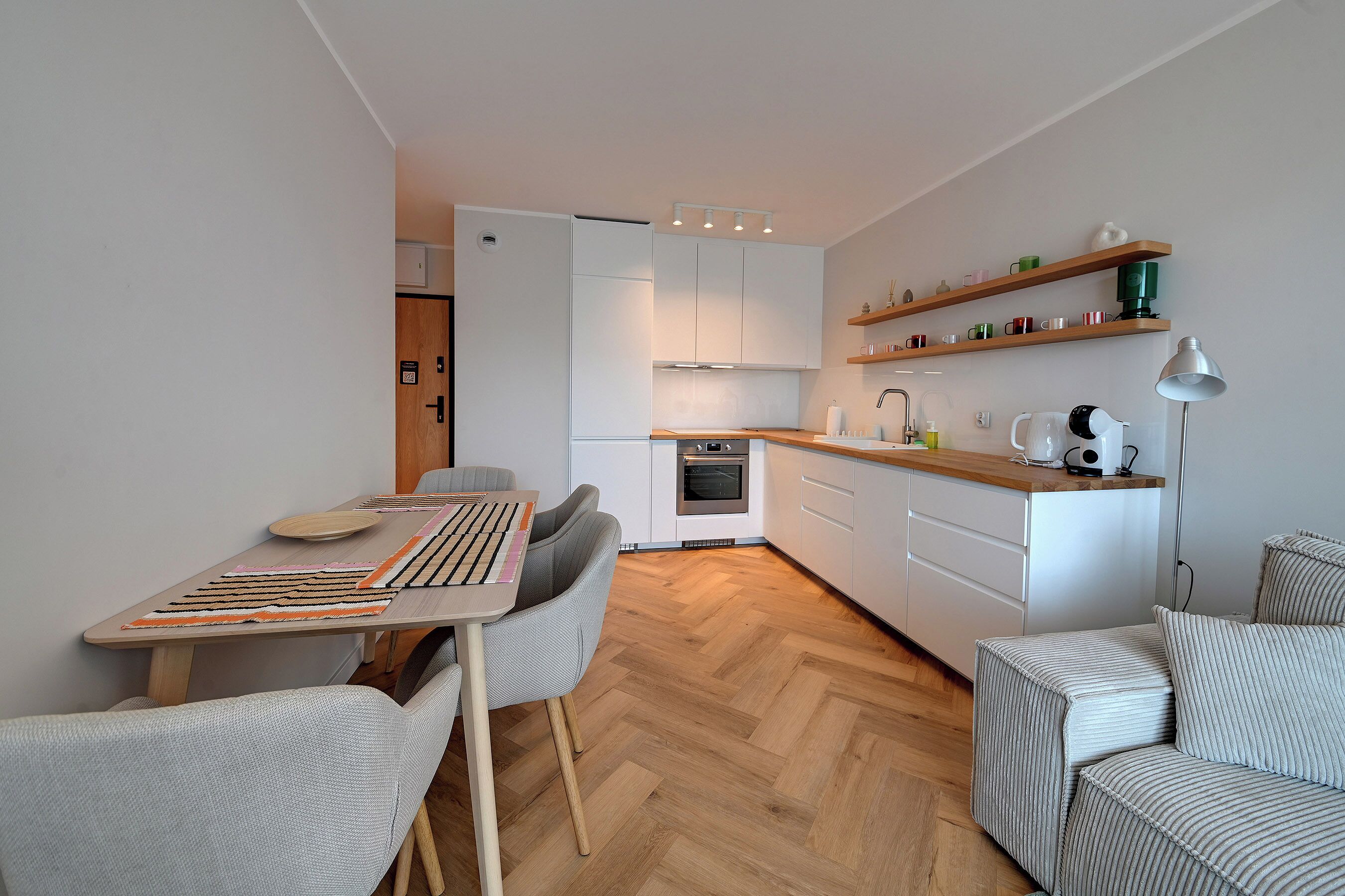 A modern kitchen with white cabinets, a wooden countertop, and a dining area with a table and chairs.