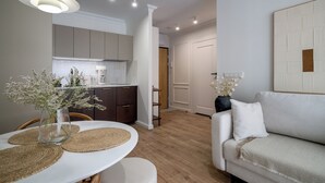 A modern living room with a white sofa, a dining table with placemats, and a kitchen in the background. - RentPlanet - Apartament Braniborska IV (Wrocław)