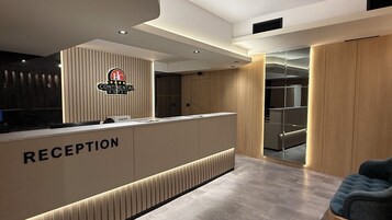Un área de recepción moderna de hotel con un mostrador de madera identificado como "RECEPTION", el logotipo de Continental Hotel y una zona de estar con una silla azul.