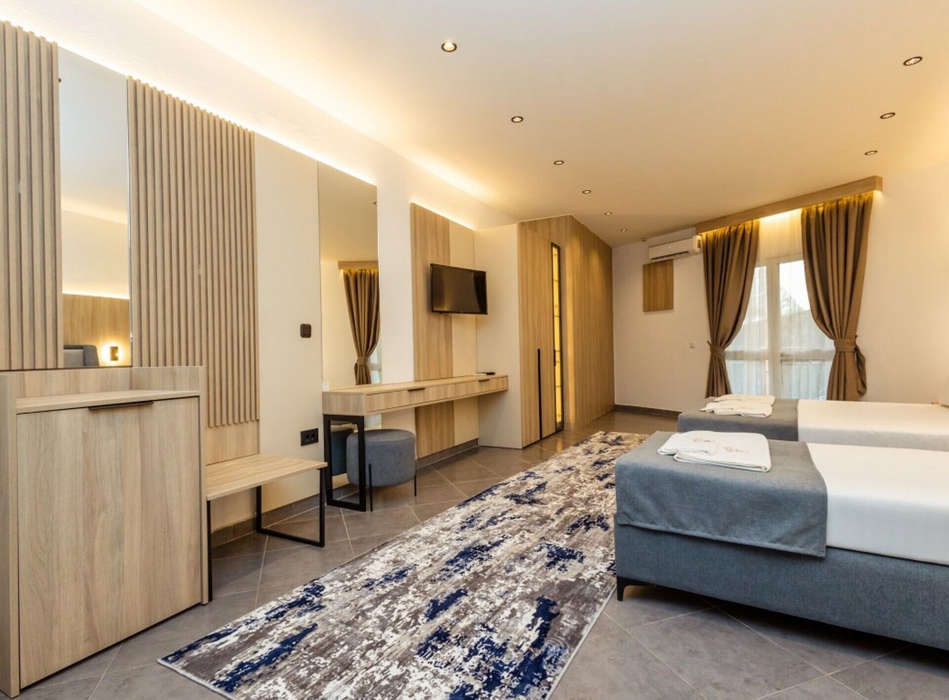A modern hotel room with a bed, a desk, a chair, a TV, and a large mirror.